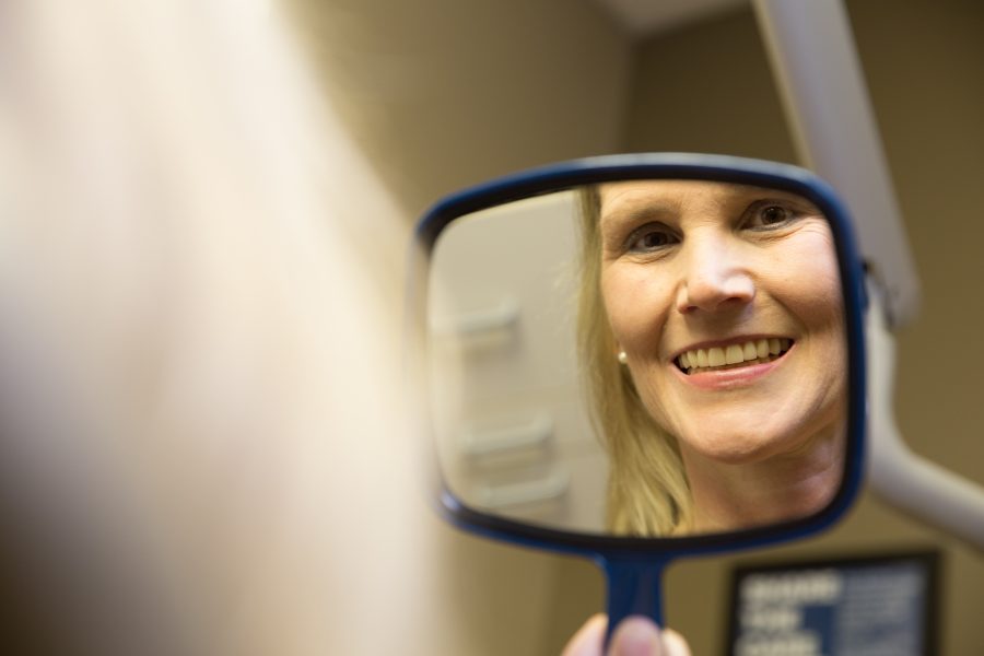 Female patient looking at her new smile in the mirror after dental implants.