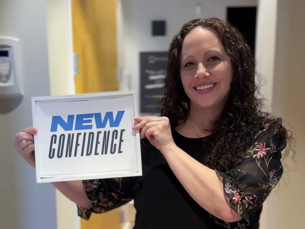 Woman holding sign and smiling with full mouth dental implants